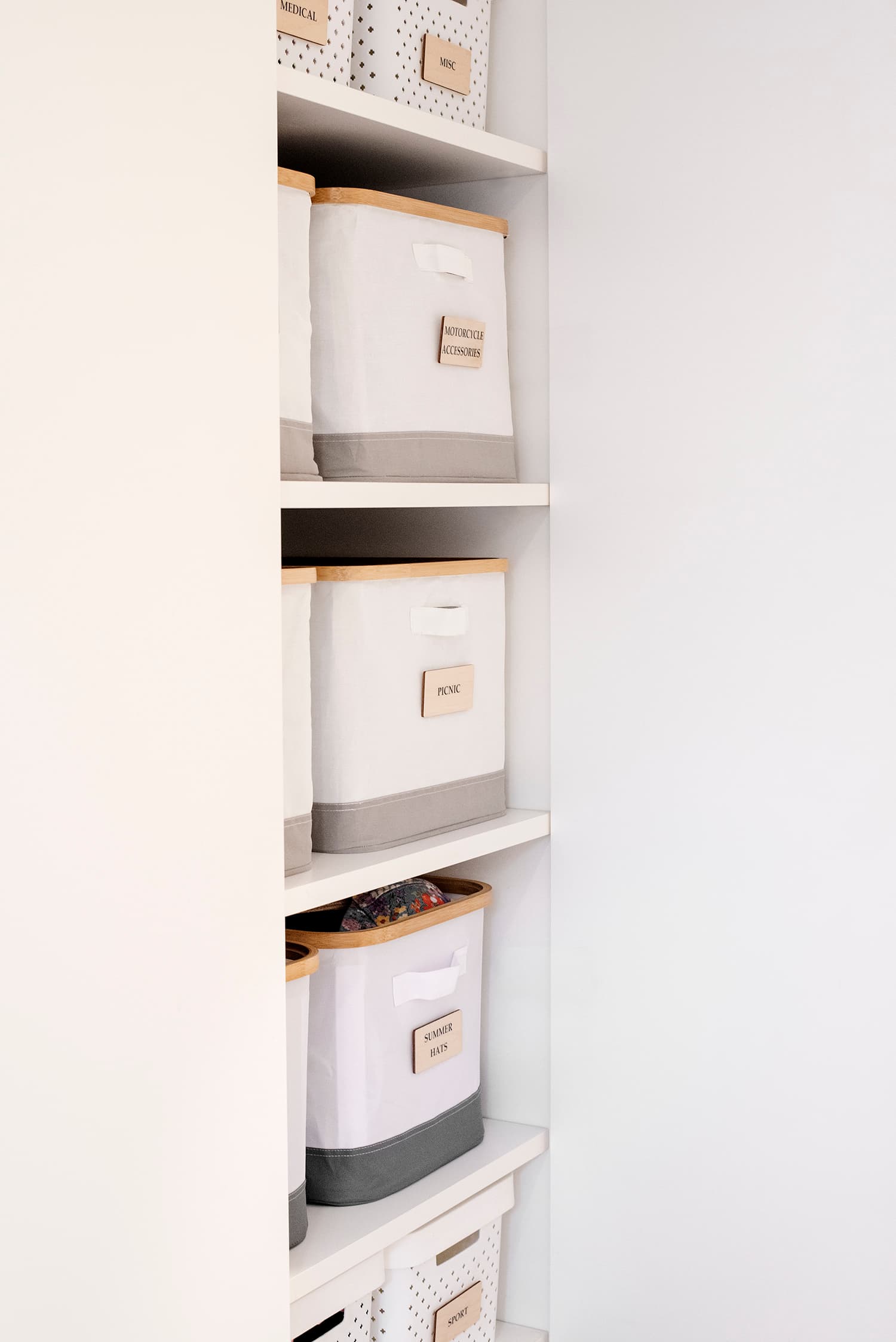 Linen cupboard shelves with labelled white and grey storage boxes.